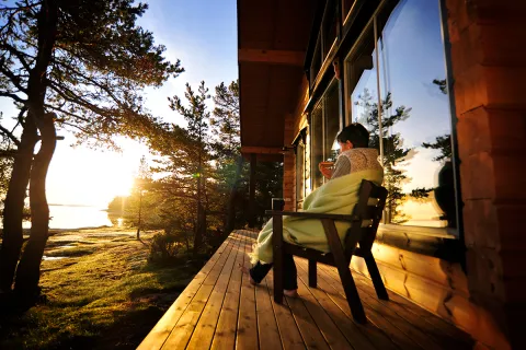 Person som njuter av morgonkaffe på altan vid stuga på Åland i soluppgången.