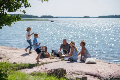 Familj som har picknick vid havet på Åland – del av resepaket med boende och upplevelser.