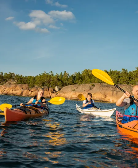 Tre personer som paddlar kajak en fin sommardag