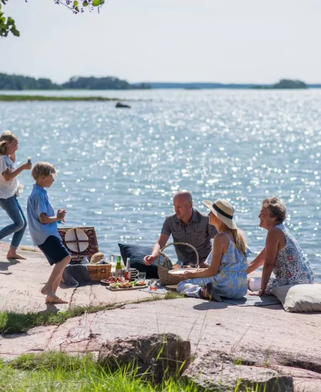 Familj som har picknick vid havet på Åland – del av resepaket med boende och upplevelser.