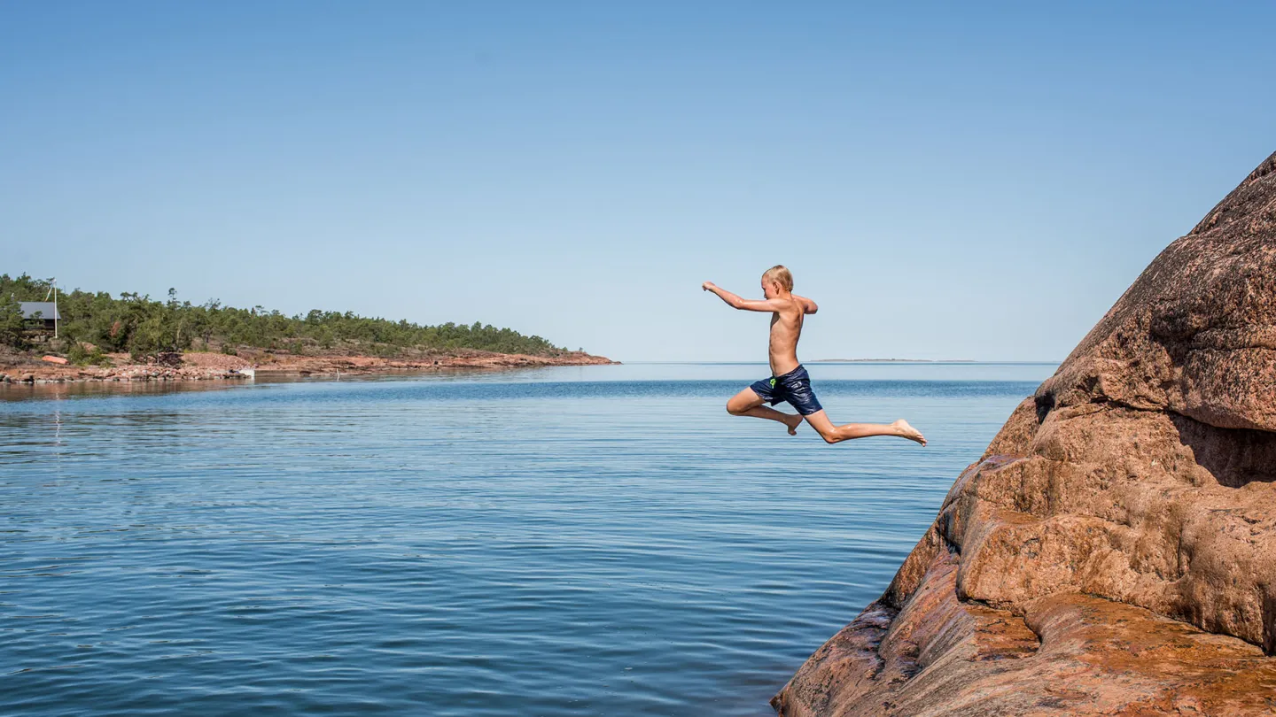 Children jumping from rocks into the sea in the Åland archipelago on a sunny summer day.