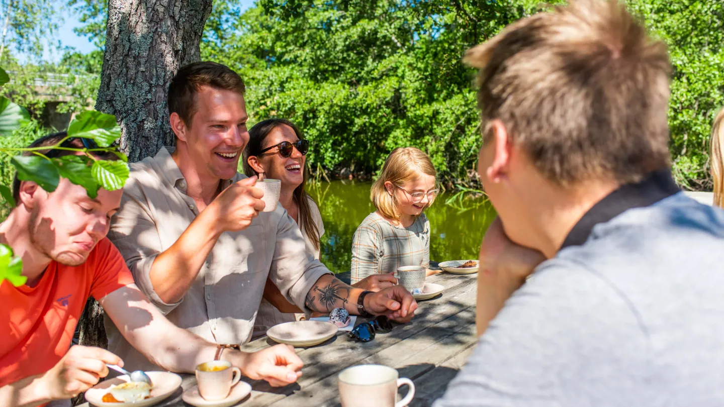 Grupp människor som sitter utomhus vid ett bord och fikar