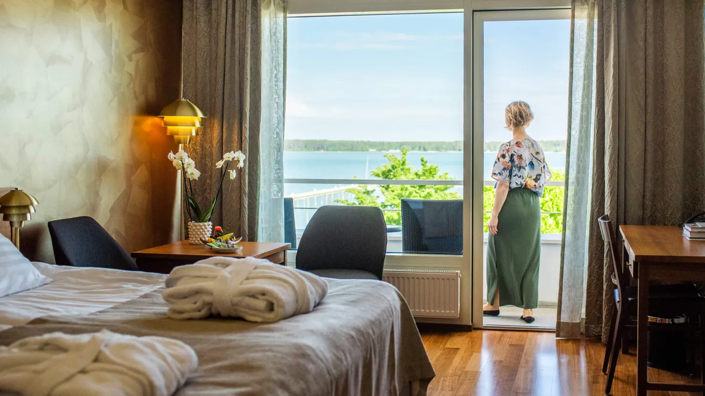 Hotel room with a balcony and sea view in Åland, where a guest looks out over the water on a sunny morning.