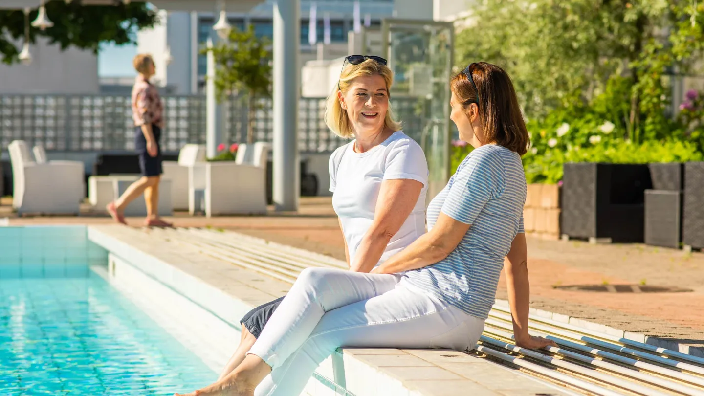 Two women relaxing by a hotel pool in Mariehamn, Åland, on a sunny summer day.