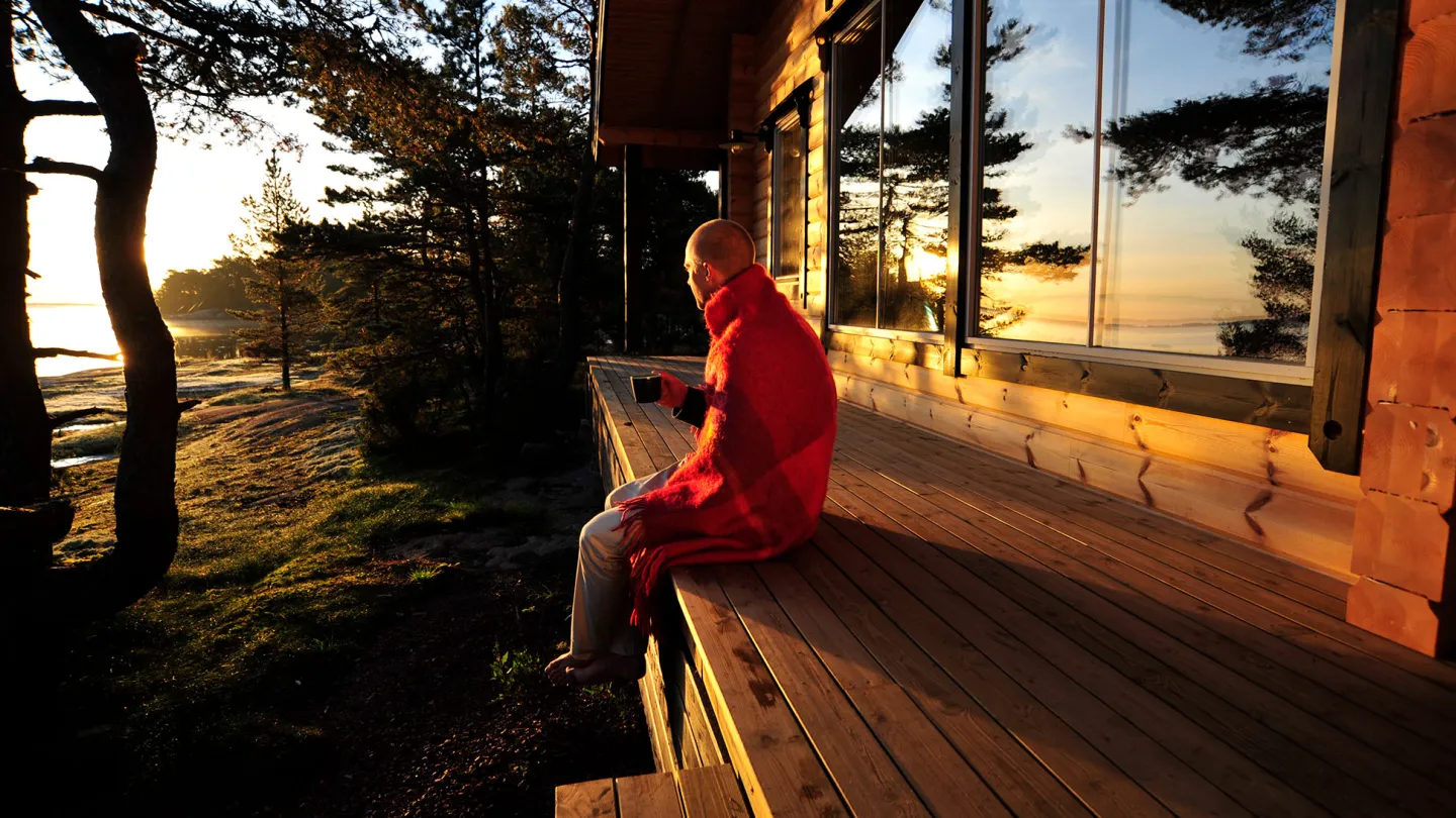 Person som sitter på stugveranda med utsikt över havet i Ålands skärgård