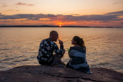 Pariskunta nauttimassa auringonlaskusta meren rannalla Ahvenanmaan punaisilla graniittikallioilla